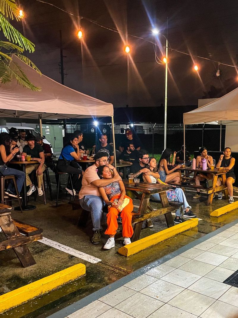 Terraza de noche con mesas tipo picnic, toldos y luces colgantes